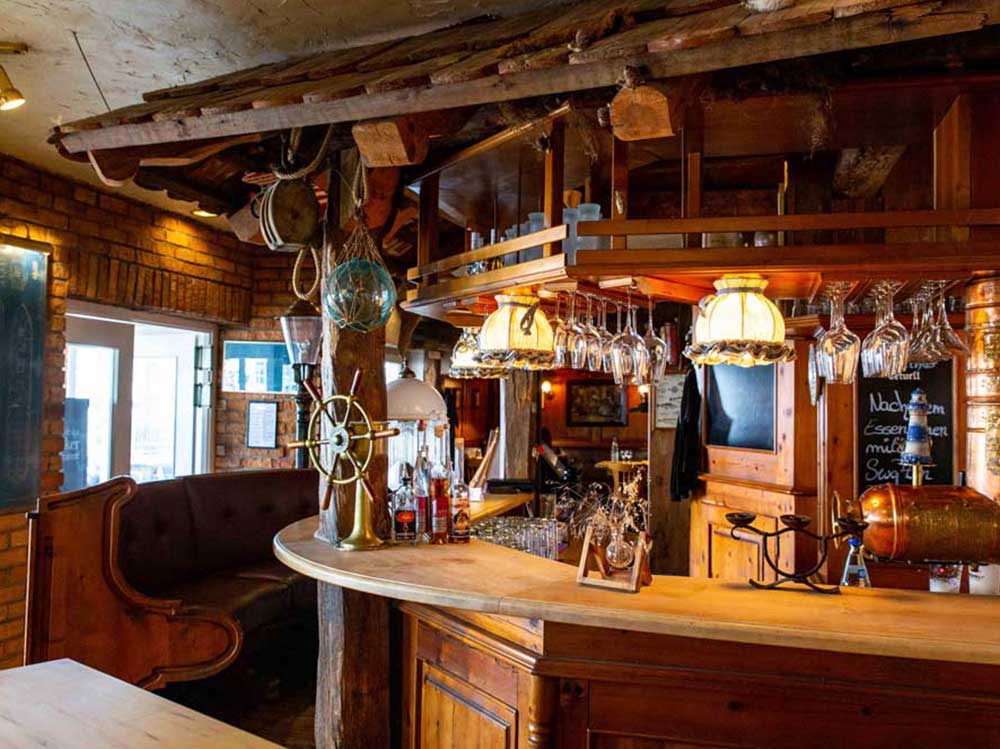 Innenansicht einer rustikalen Bar mit Holzeinrichtung, Hängelampen und Gläsern, gemütliche Atmosphäre